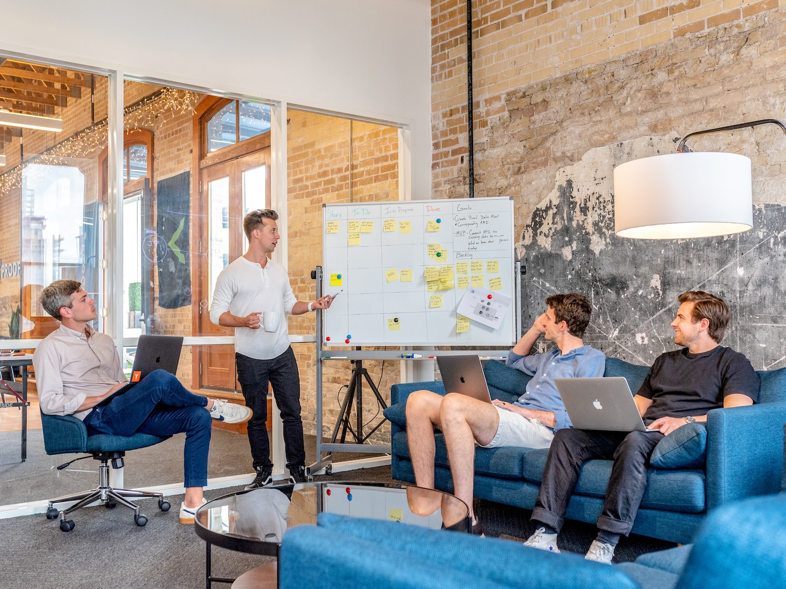 Photo by Austin Distel three men sitting while using laptops and watching man beside whiteboard
